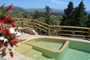 A pool with a wooden deck and stone steps, surrounded by greenery and a scenic view. - Spectacular Stone Villa with Pool in Forest and Great Sea & Mountain Views (Chania crete)
