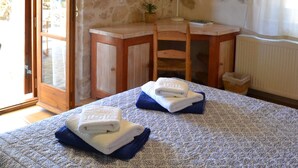 Ein Schlafzimmer mit Steinwand, Holzboden, einem Bett mit gemustertem Überwurf, einem Schreibtisch mit Stuhl, einer Hängeleuchte und einem Fenster mit Vorhängen.