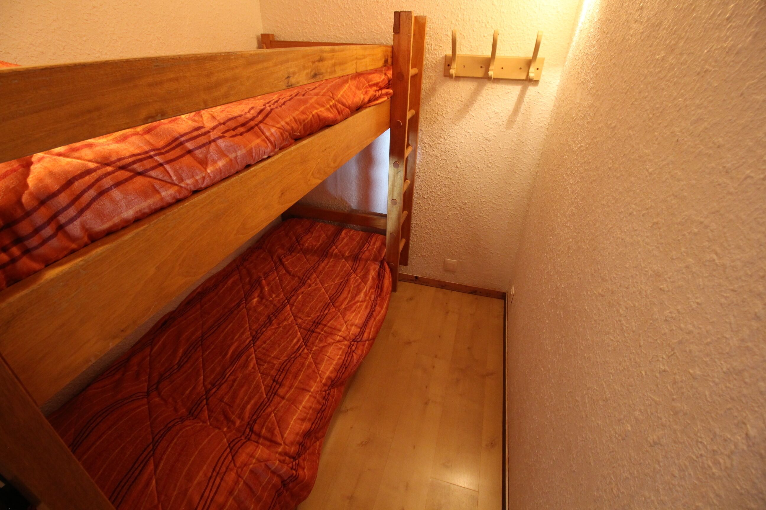 A bunk bed with a plaid blanket, wooden headboard, and a wall-mounted shelf.