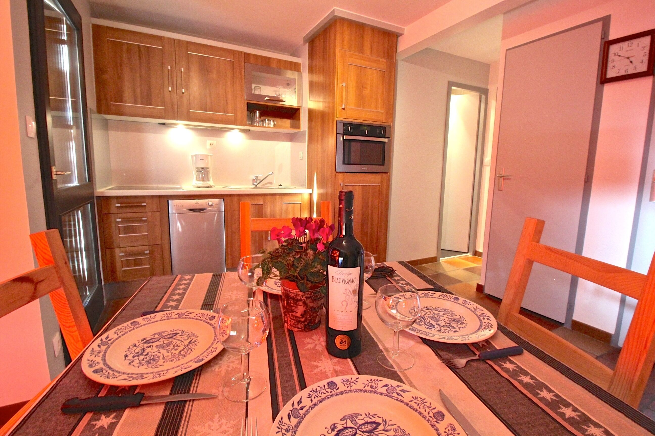 A dining area with a table set for two, a bottle of wine, and a potted plant.