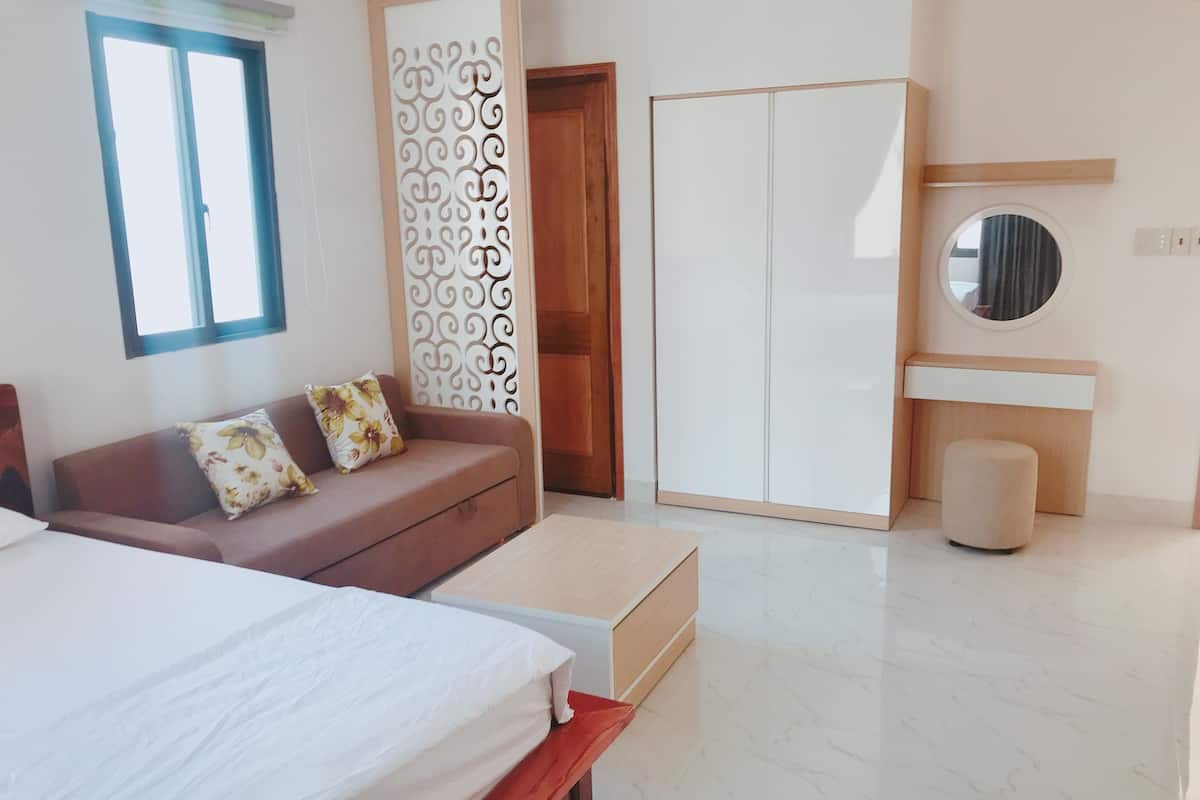 Un dormitorio moderno con cama, sofá, armario, espejo y una pequeña mesa redonda.