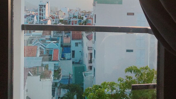 Vista a través de una ventana que muestra un paisaje urbano con edificios y una cadena montañosa distante.