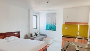 Habitación de hotel con cama, sofá, pequeña cocina y ventana con vistas.