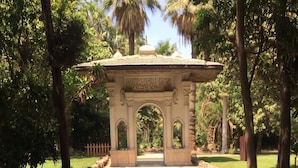 A paved pathway leading to an ornate archway with a dome, surrounded by trees and a fence. - Arabian Nights Pyramids Guesthouse (Giza)