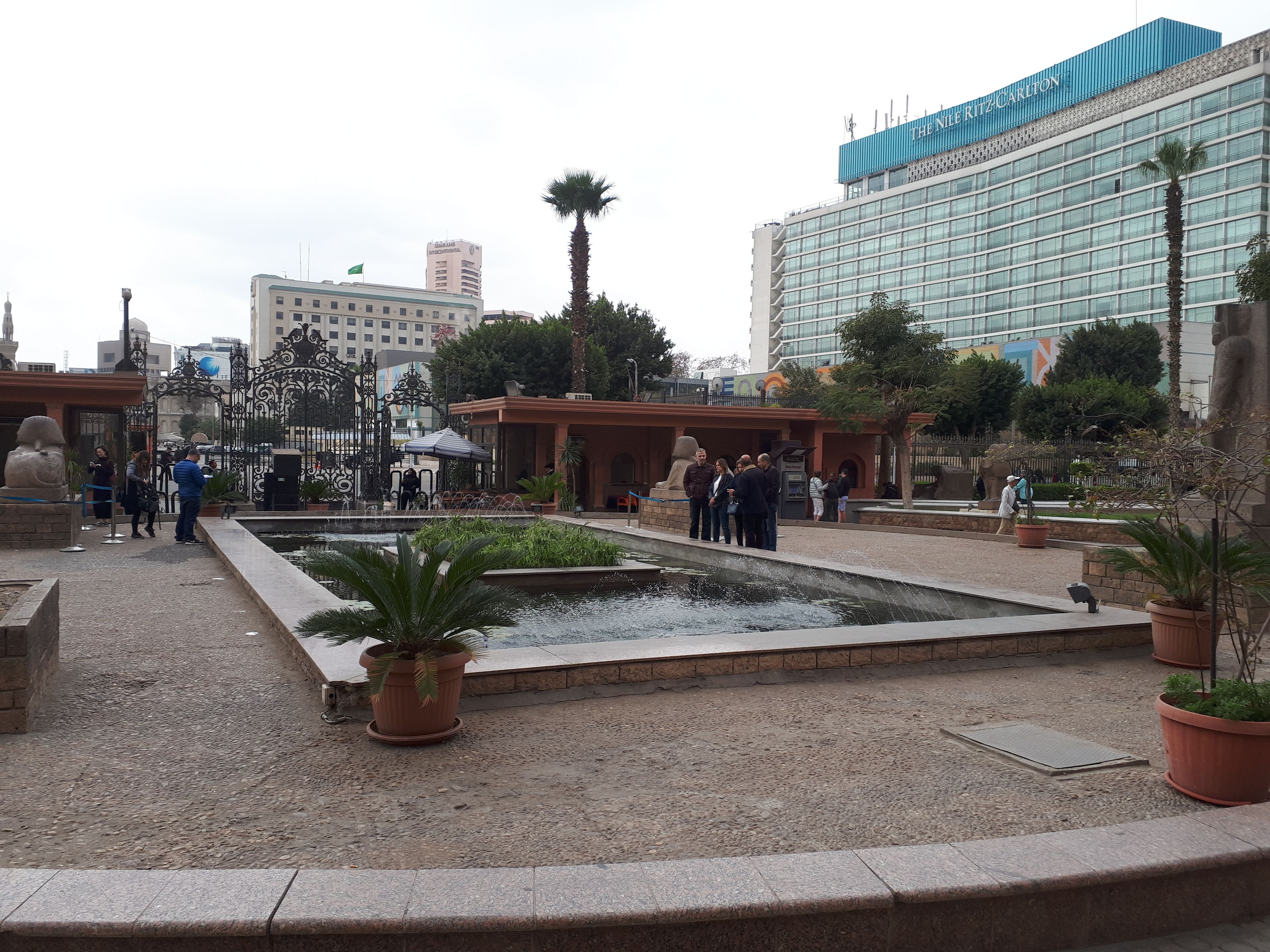 A courtyard with a fountain, potted plants, and a group of people.