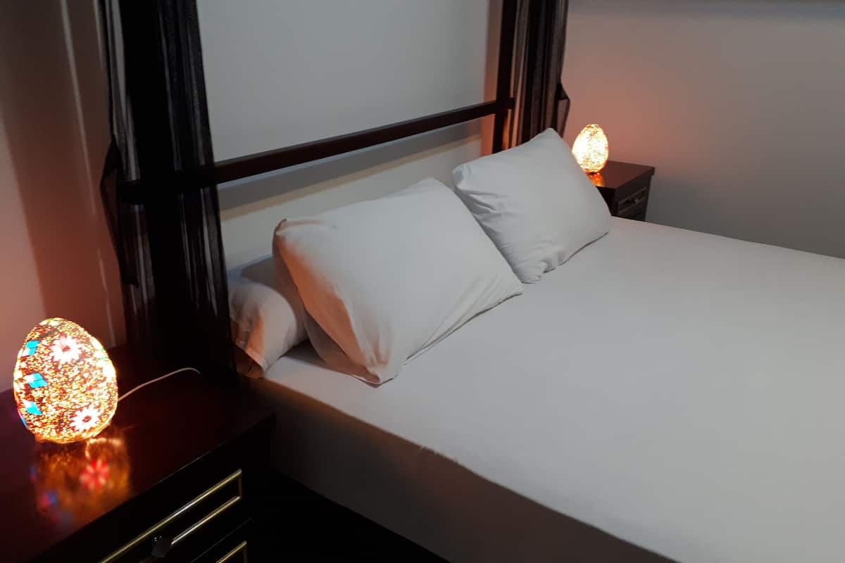 A neatly made bed with white linens and pillows, a dark headboard, and two bedside lamps with decorative lights.
