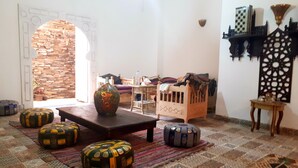 A cozy living room with a stone wall, a wooden table, colorful cushions, and a decorative vase. - Arabian Nights Pyramids Guesthouse (Giza)