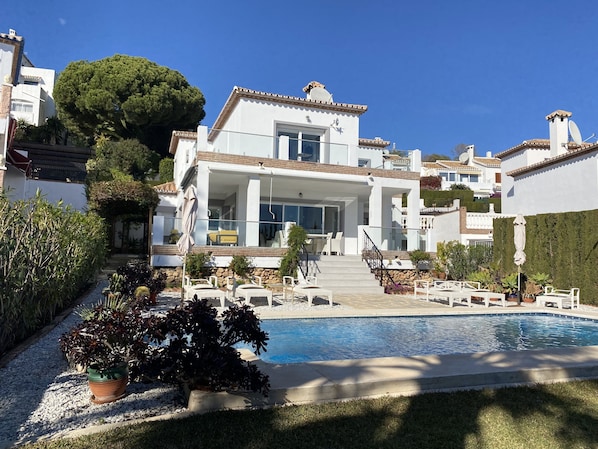Une maison moderne à deux étages, dotée d’une piscine, d’un espace de détente extérieur et d’un jardin bien entretenu.