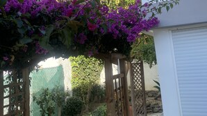 A garden with a pergola covered in purple bougainvillea, a white building with a tiled roof, and a stone wall. - villa halcyon 24 calle huelva calahonda (Mijas)