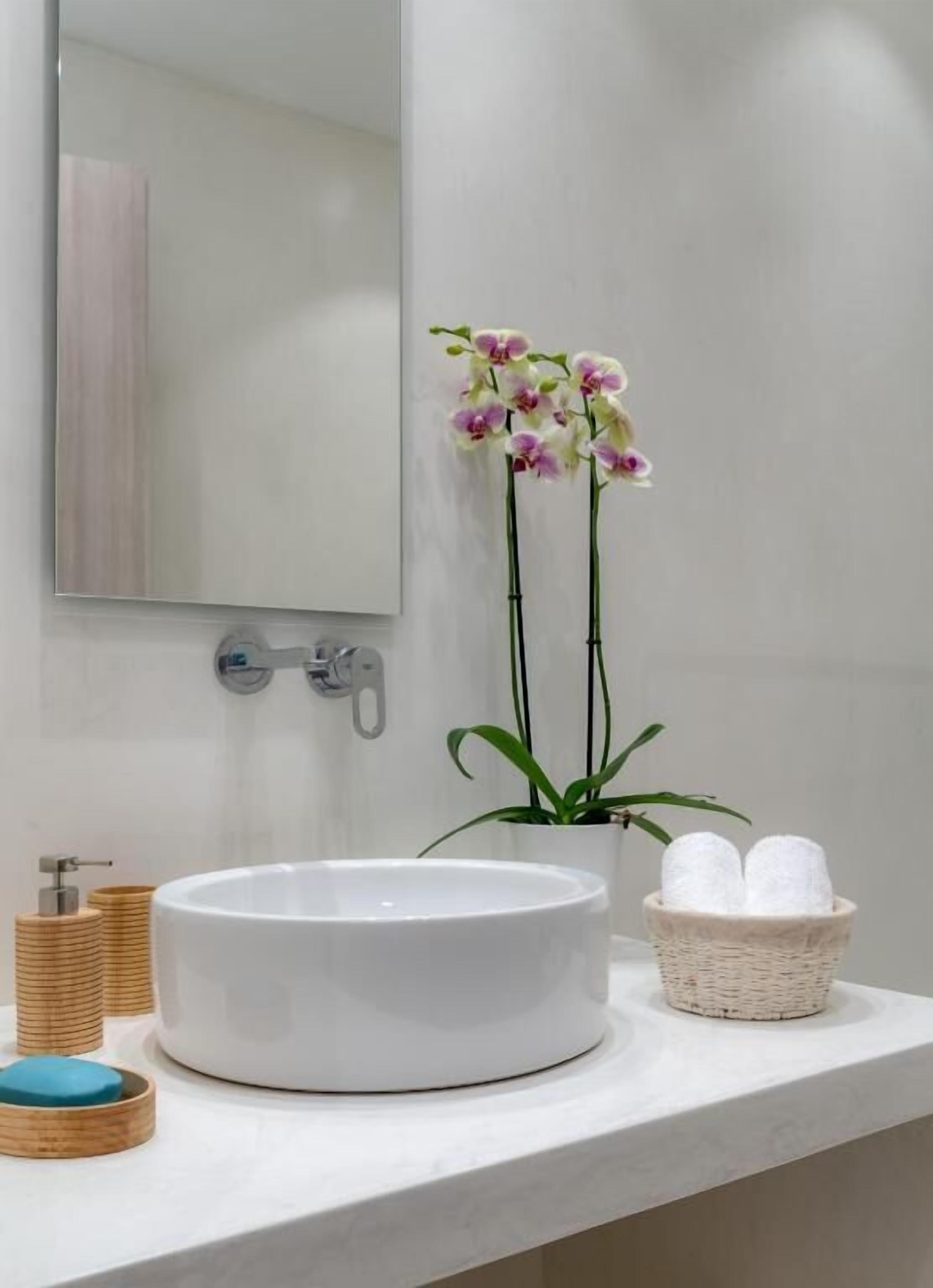 A bathroom with a round white sink, a mirror, a potted plant, and a basket of towels.