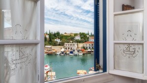 A view from a window overlooking a marina with boats docked, buildings in the background, and a clear sky. - Porto Vecchio Luxury Suites (Spetses)