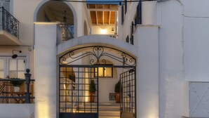A white building with a gated entrance, steps leading to a covered area, and potted plants on either side. - Porto Vecchio Luxury Suites (Spetses)