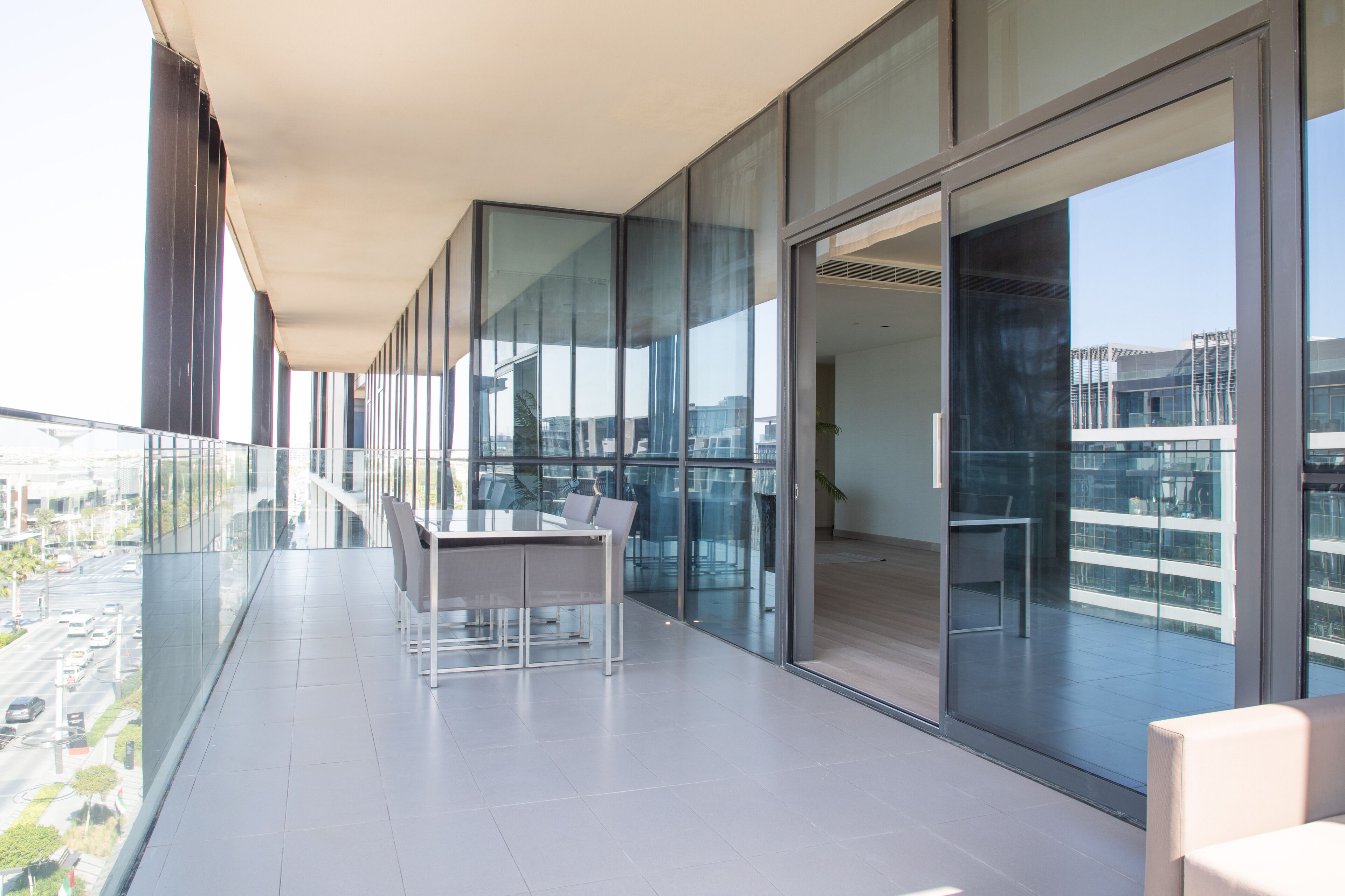 Ein moderner Balkon mit Glasgeländer, Tisch und Stühlen mit Blick auf eine Stadtlandschaft.