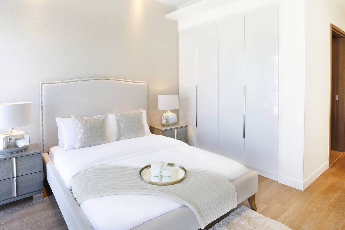 Un dormitorio moderno con una cama grande, lámparas de noche, una bandeja con tazas y un armario.