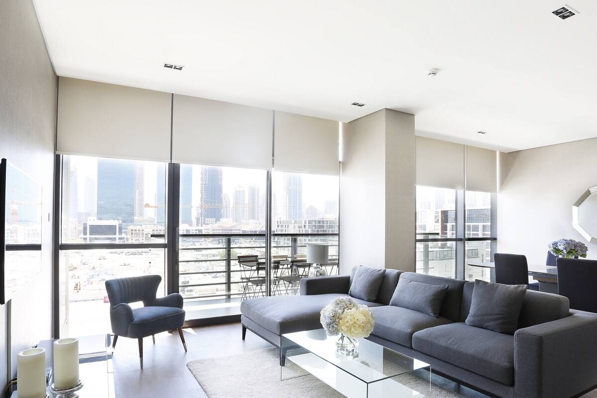 Una sala de estar moderna con un sofá gris, una mesa de centro de vidrio y vistas de la ciudad a través de amplias ventanas.