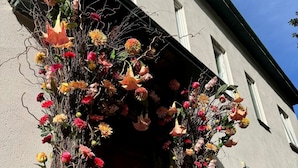 L’entrée d’un immeuble, avec une porte en bois et une composition florale au-dessus.