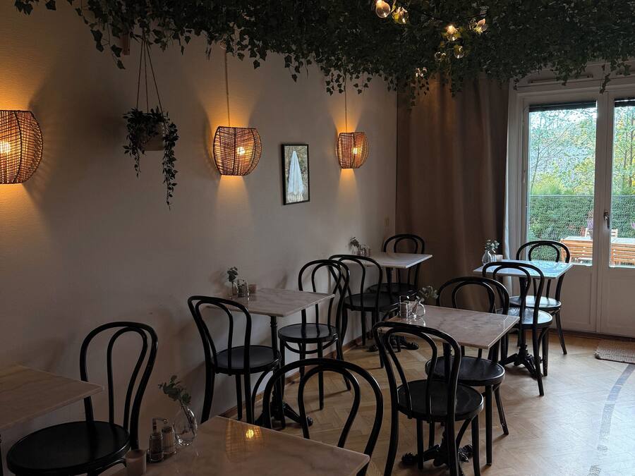 Un restaurante con mesas de madera y sillas negras, plantas colgantes e iluminación empotrada en la pared.