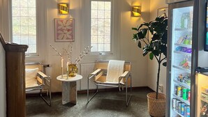 Une pièce dotée d’un plafond au design moderne, d’un coin salon avec une table et des chaises, d’un luminaire fixé au mur et d’un réfrigérateur rempli de boissons.