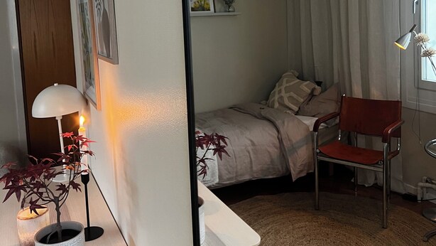 Une chambre à coucher avec un lit, une chaise, un bureau avec une lampe et une plante en pot.