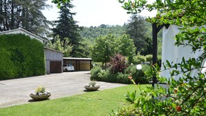 Un jardin bien entretenu, avec une allée pavée menant à un garage, le tout entouré d’une végétation luxuriante et agrémenté d’une voiture blanche garée à l’intérieur.