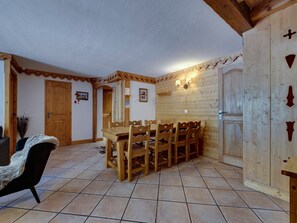 Un comedor con mesa y sillas de madera, suelo de baldosas y paredes de madera con detalles decorativos.