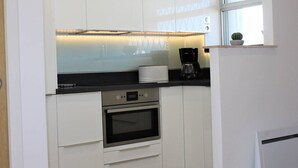 A modern kitchen with white cabinets, a black countertop, a built-in oven, a coffee maker, and a window with a cactus plant.