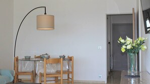 A dining area with a table, chairs, and a lamp. There is a vase with flowers on a table to the right.