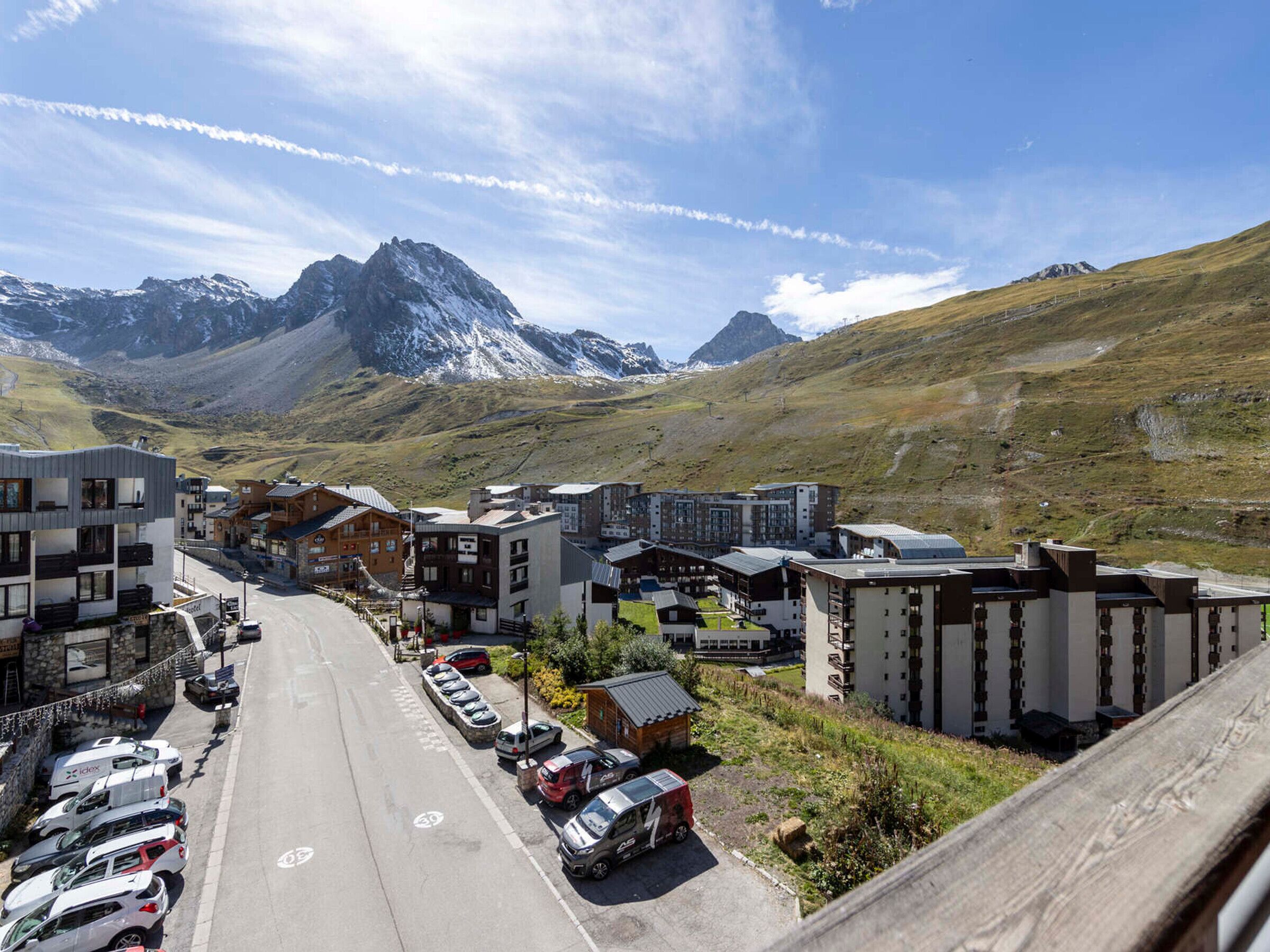 En bergsstad med moderna byggnader, en parkeringsplats och utsikt över snöklädda bergstoppar.