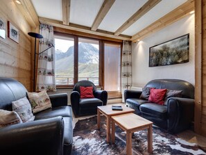 A cozy room with two leather sofas, a wooden coffee table, and a cowhide rug. Large windows offer a mountain view.
