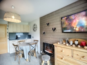 Een moderne keuken met houten kastjes, een eettafel met stoelen, een open haard en decoratieve muurkunst.