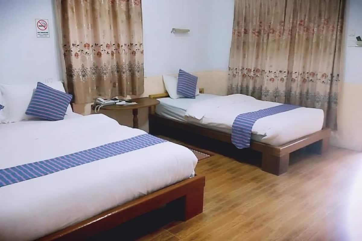 Habitació d'hotel amb dos llits individuals, ambres de fusta, una tauleta de nit, una làmpada i una finestra amb cortines.