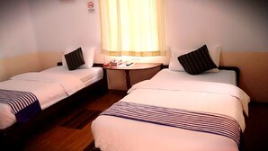 Een hotelkamer met twee eenpersoonsbedden, een klein rond tafeltje en een raam met gordijnen.