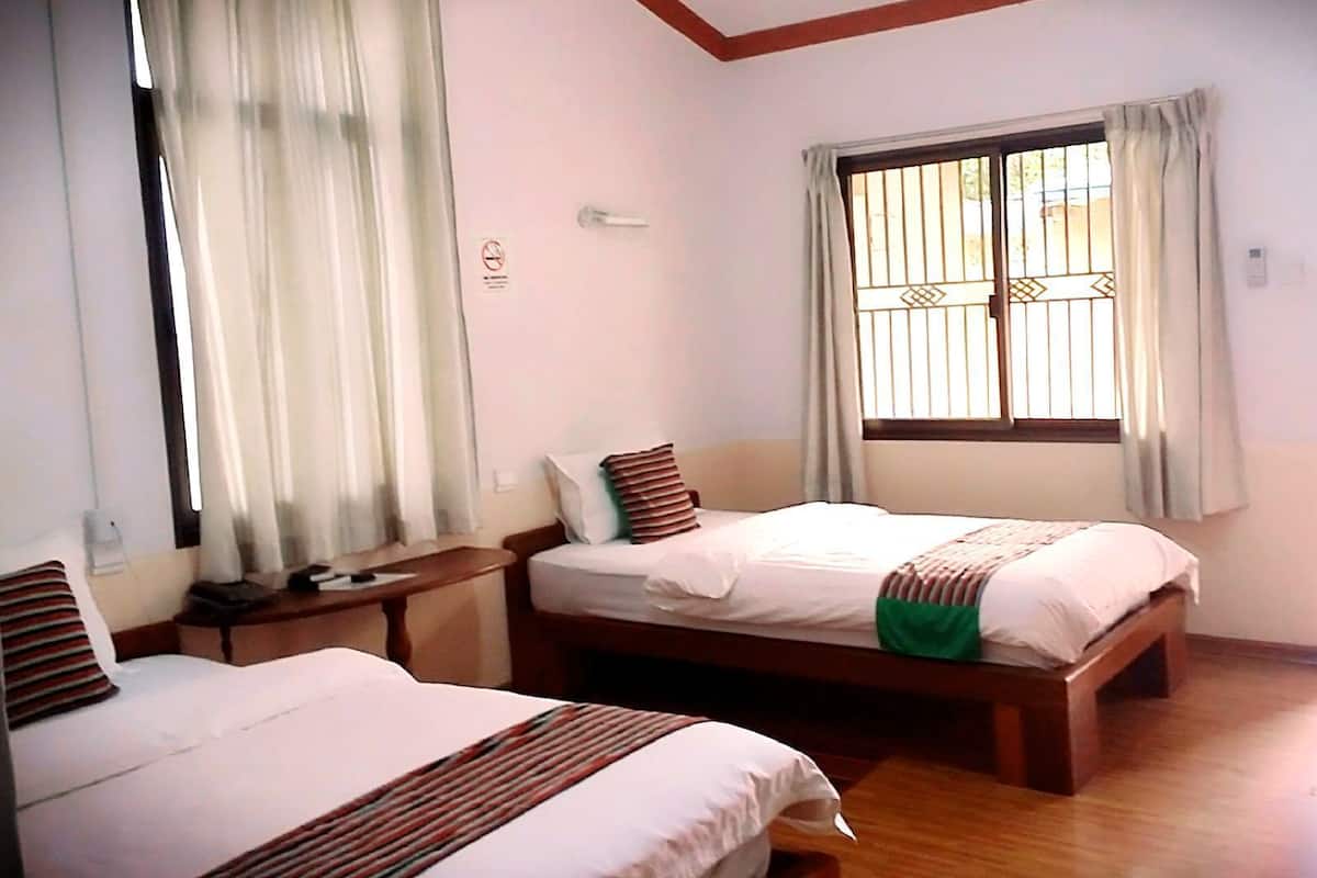 Habitació d'hotel amb dos llits, una finestra amb reixes metàl·liques, un paviment de fusta i una taula de nit amb una làmpada.
