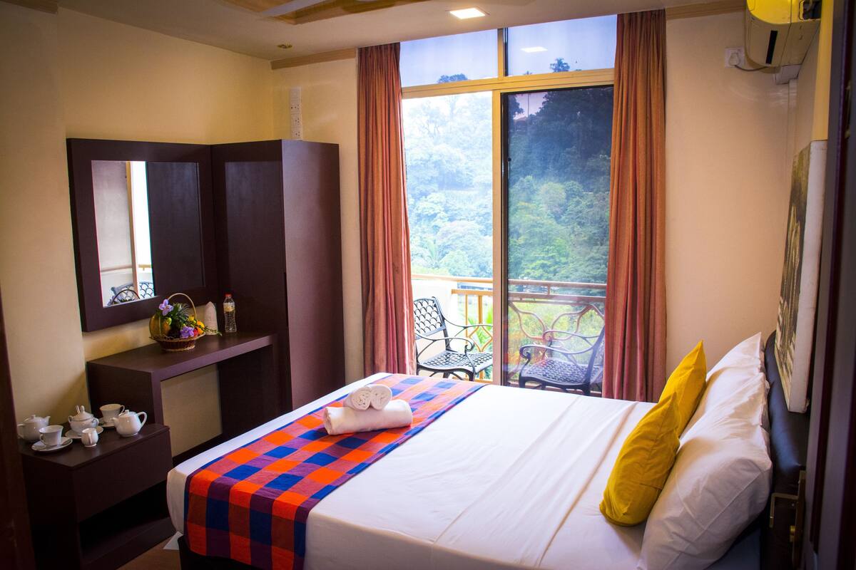 Habitación de hotel con cama, escritorio con tetera, ventana con cortinas y balcón con sillas.