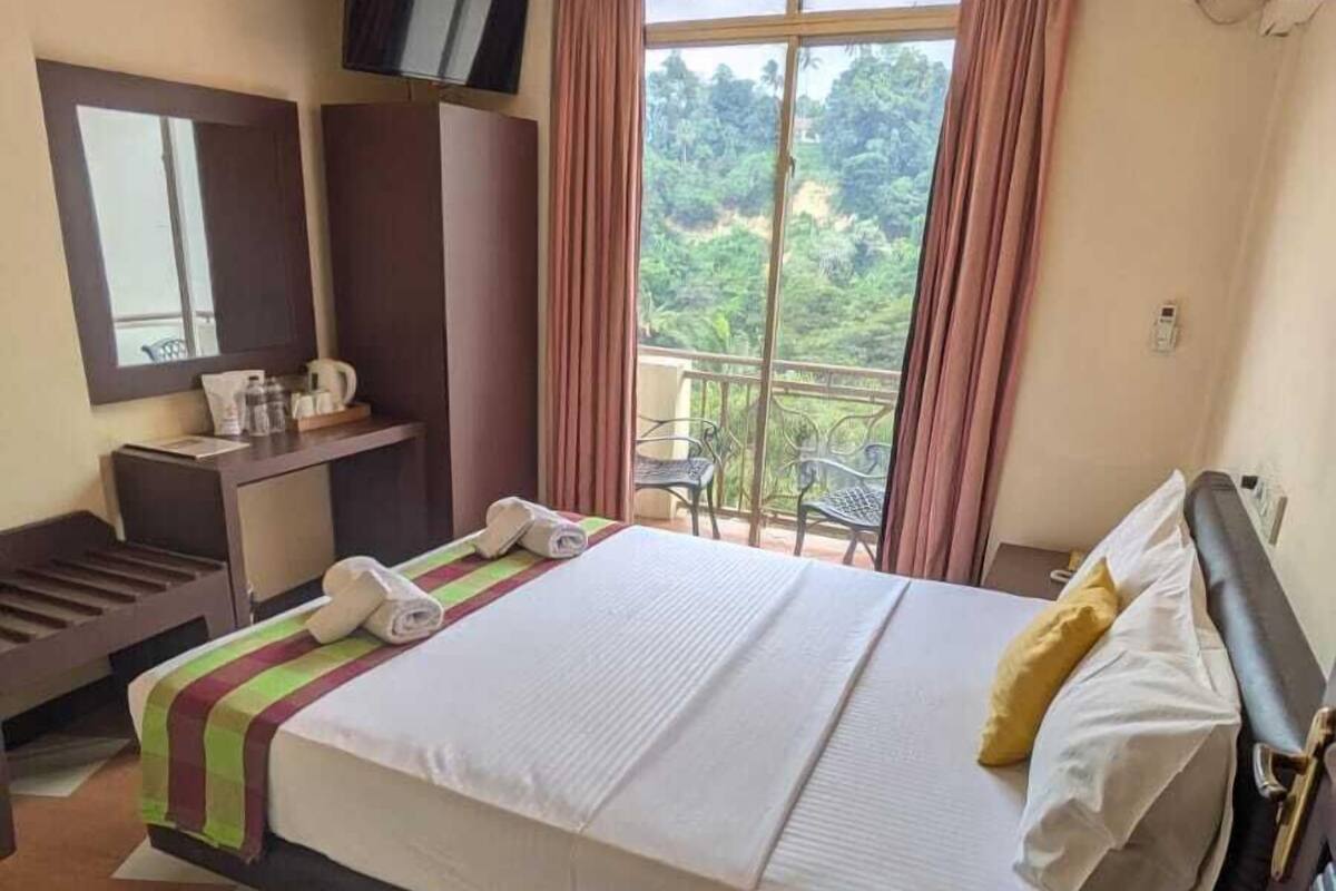 Habitación de hotel con una cama grande, un escritorio con silla, televisión y un balcón con cortinas.