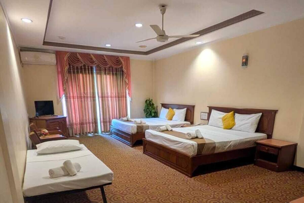 Habitación de hotel con dos camas, un escritorio, una silla, ventilador de techo y alfombra estampada.