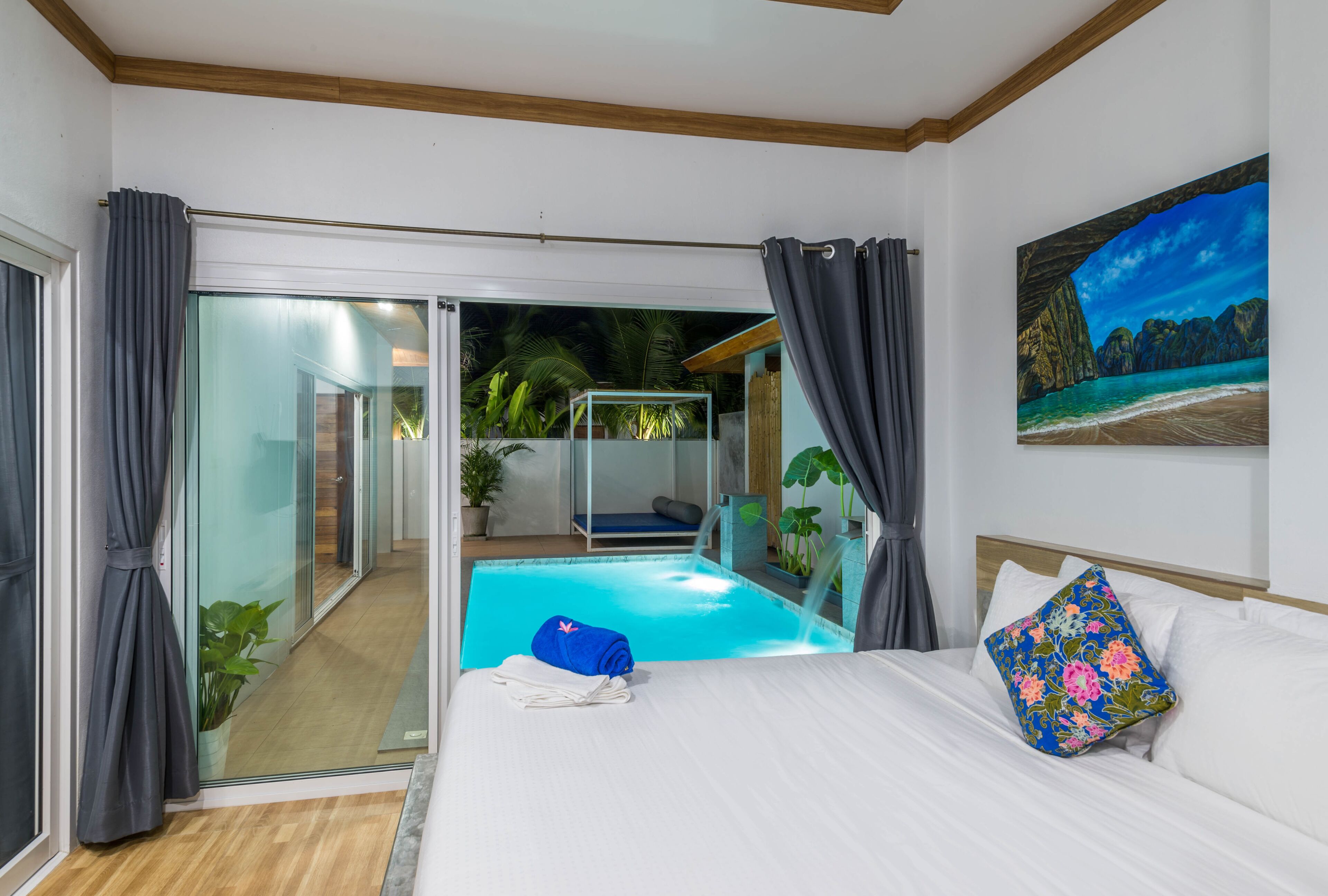 A hotel room with a bed, a painting, a window with curtains, a small pool, and a view of the outside.