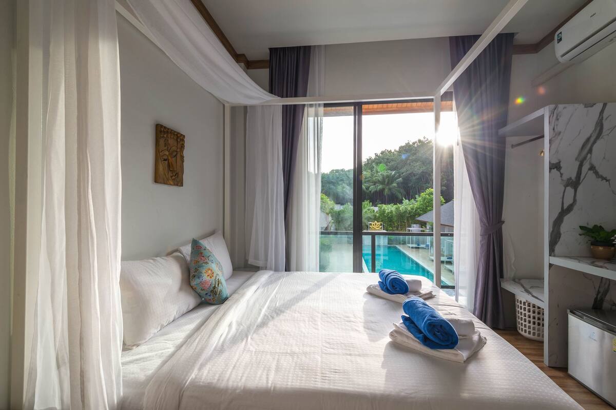 Une chambre d’hôtel avec un grand lit, une vue sur une piscine et un balcon avec des rideaux.