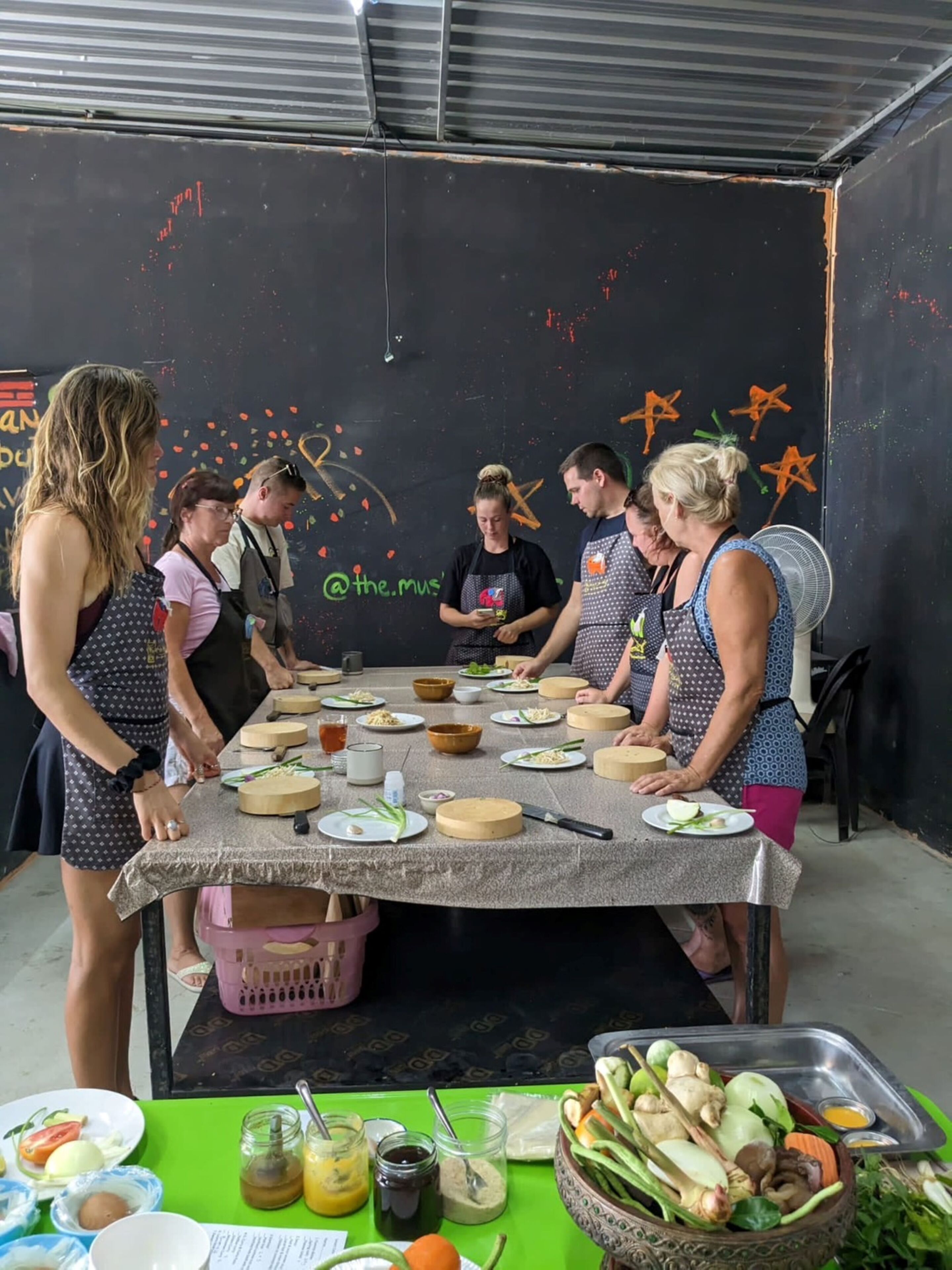 Un grupo de personas preparando comida alrededor de una mesa con diversos ingredientes y utensilios.