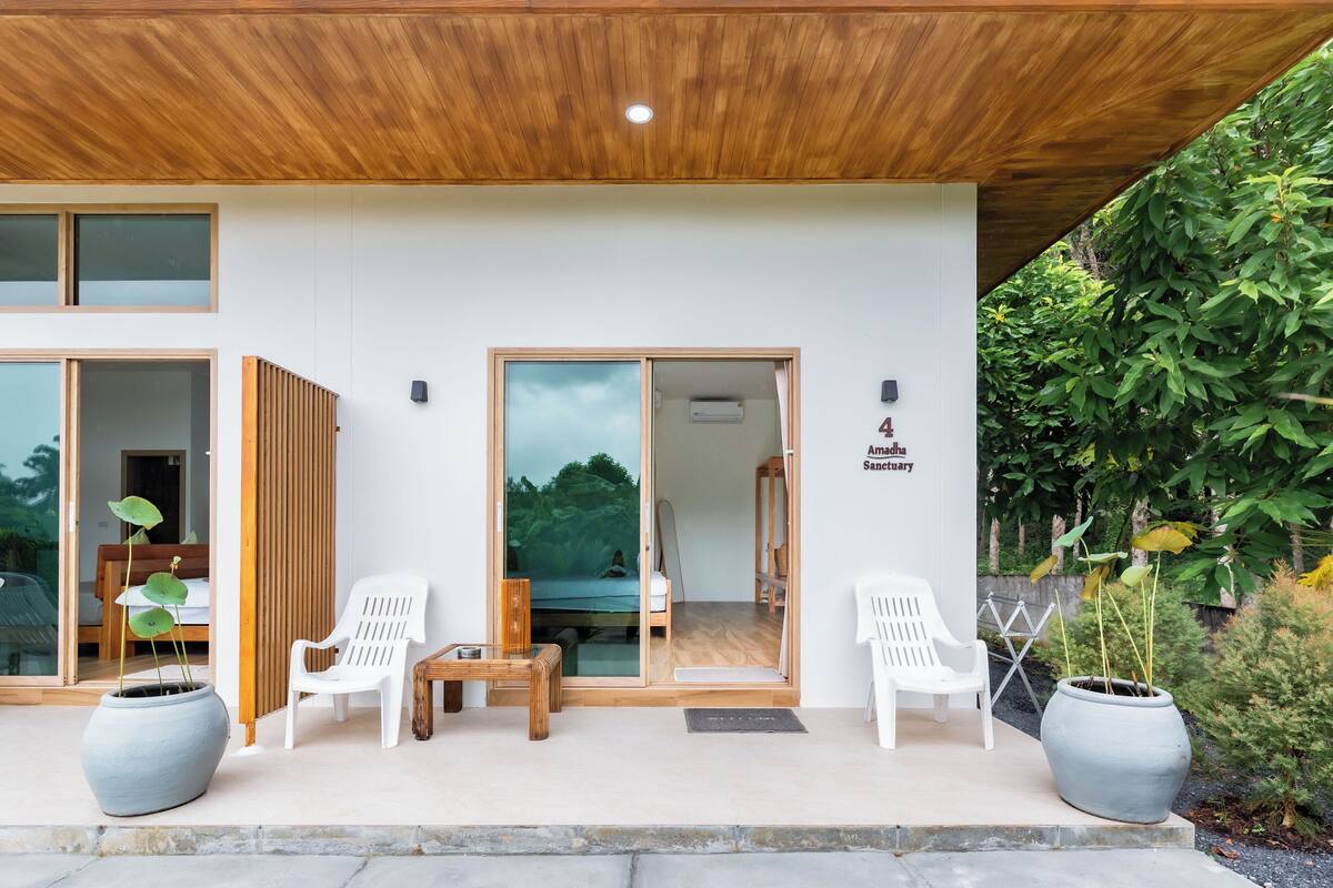Un bâtiment moderne avec un plafond en bois, de grandes portes vitrées, des chaises blanches et des plantes en pot.