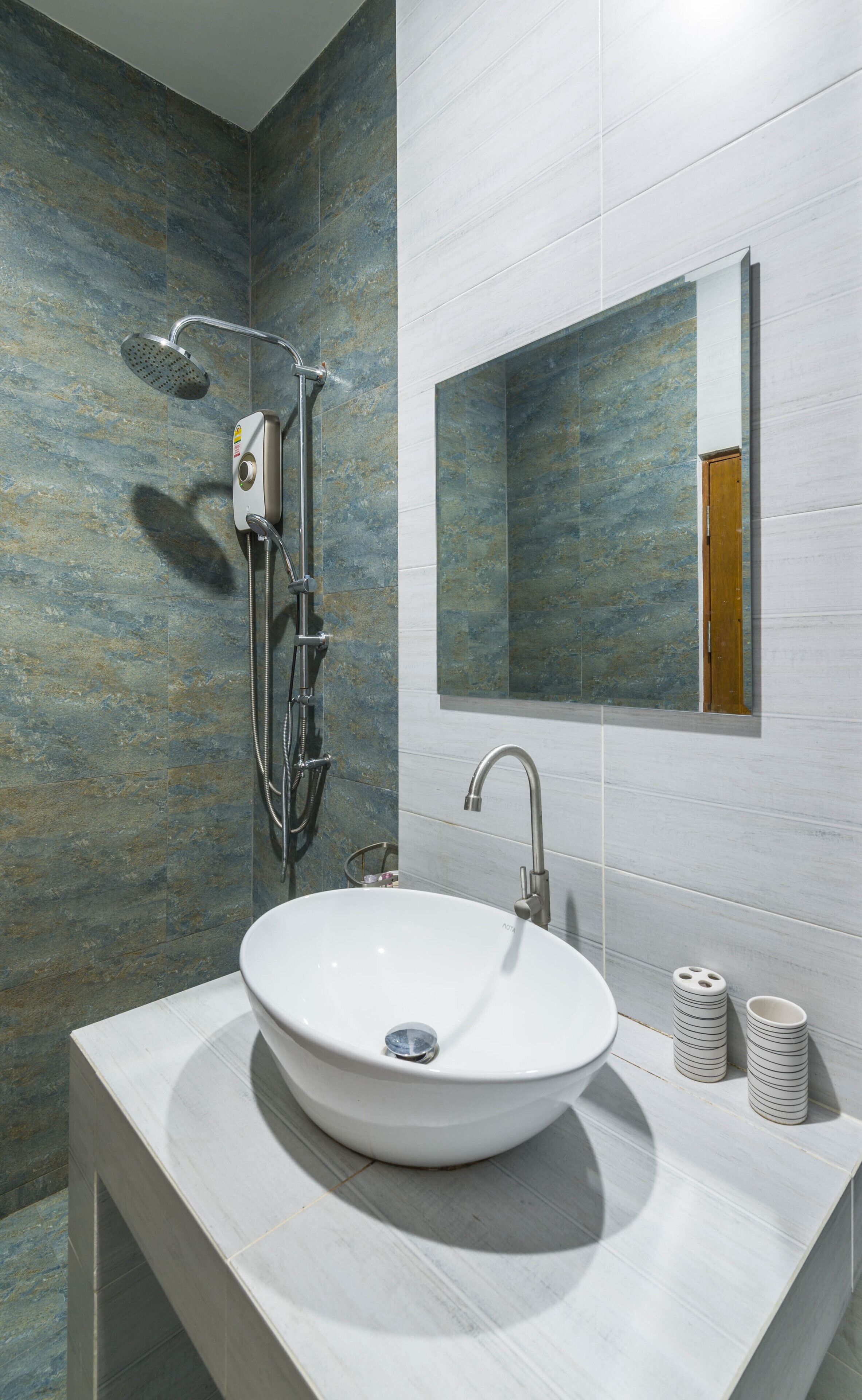 Un baño moderno con un lavamanos grande de color blanco, un cabezal de ducha de mano y un espejo montado en la pared.