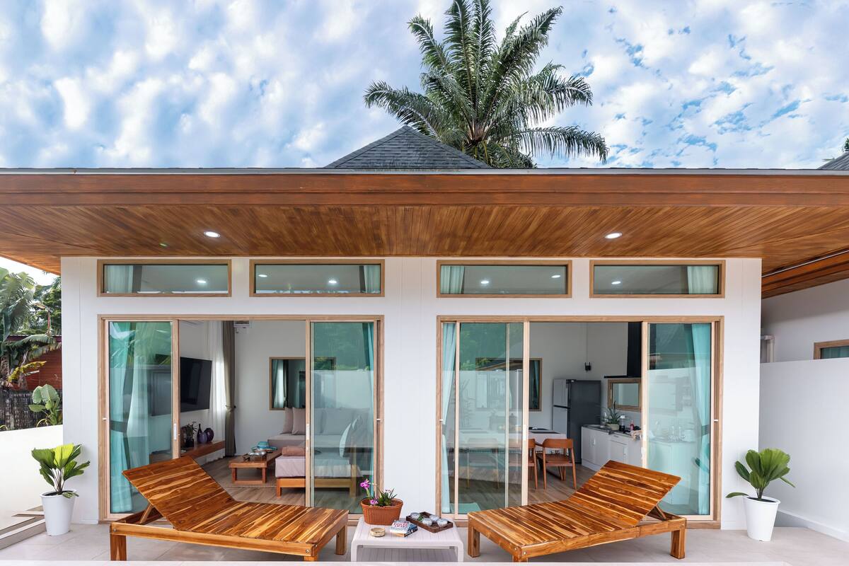 Une maison moderne avec un toit en bois, de grandes portes vitrées et un balcon agrémenté de meubles en bois.