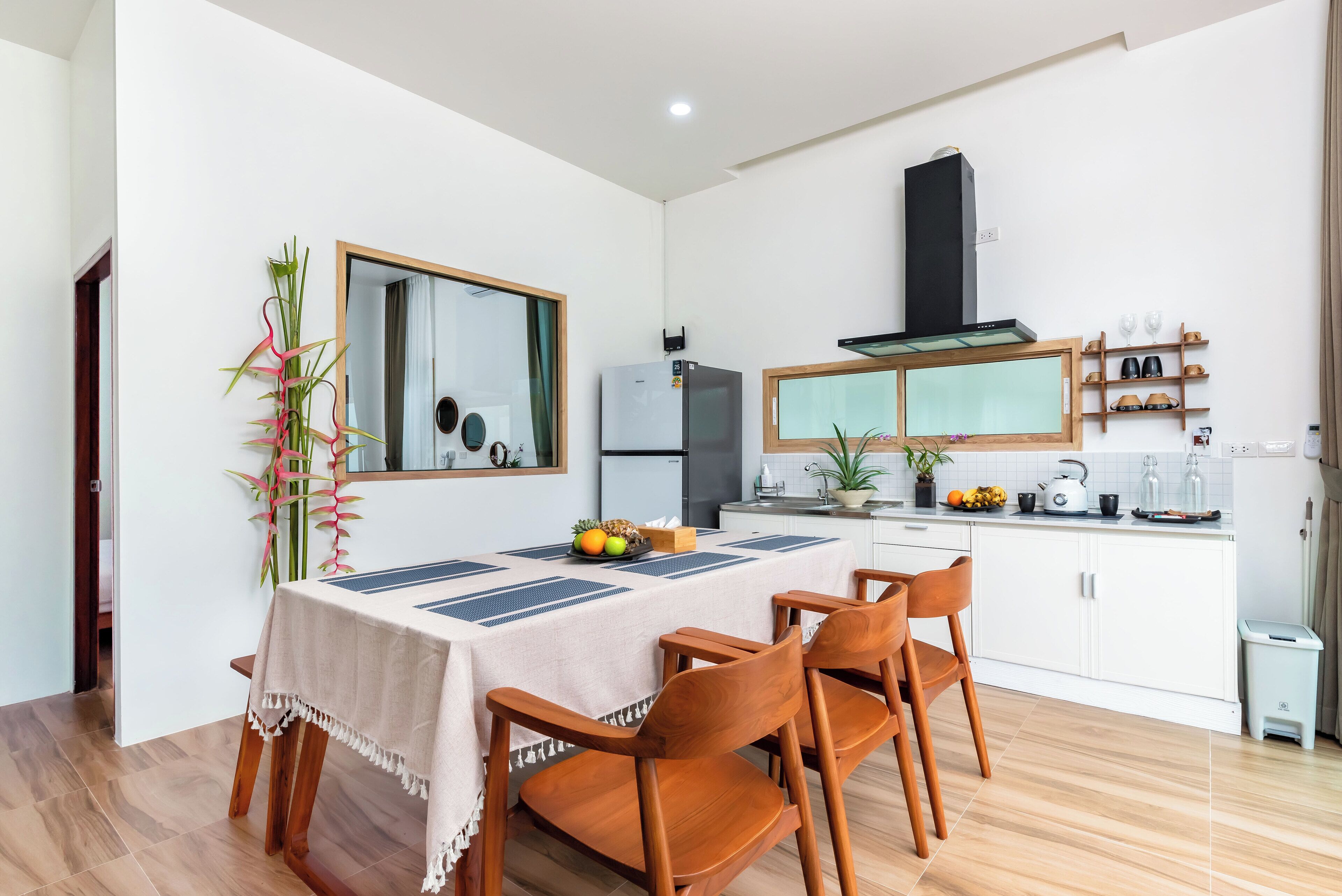 A modern kitchen with white cabinets, a built-in oven, and a microwave. There is a dining table with chairs and a vase of flowers.