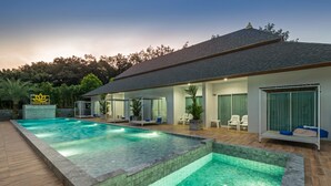 Ett modernt hus med en stor swimmingpool, en täckt uteplats med sittplatser och en skylt med en lotusblomsymbol.
