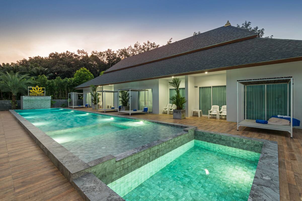 Une maison moderne dotée d’une grande piscine, d’un patio couvert avec des sièges et d’un panneau orné d’un symbole de lotus.