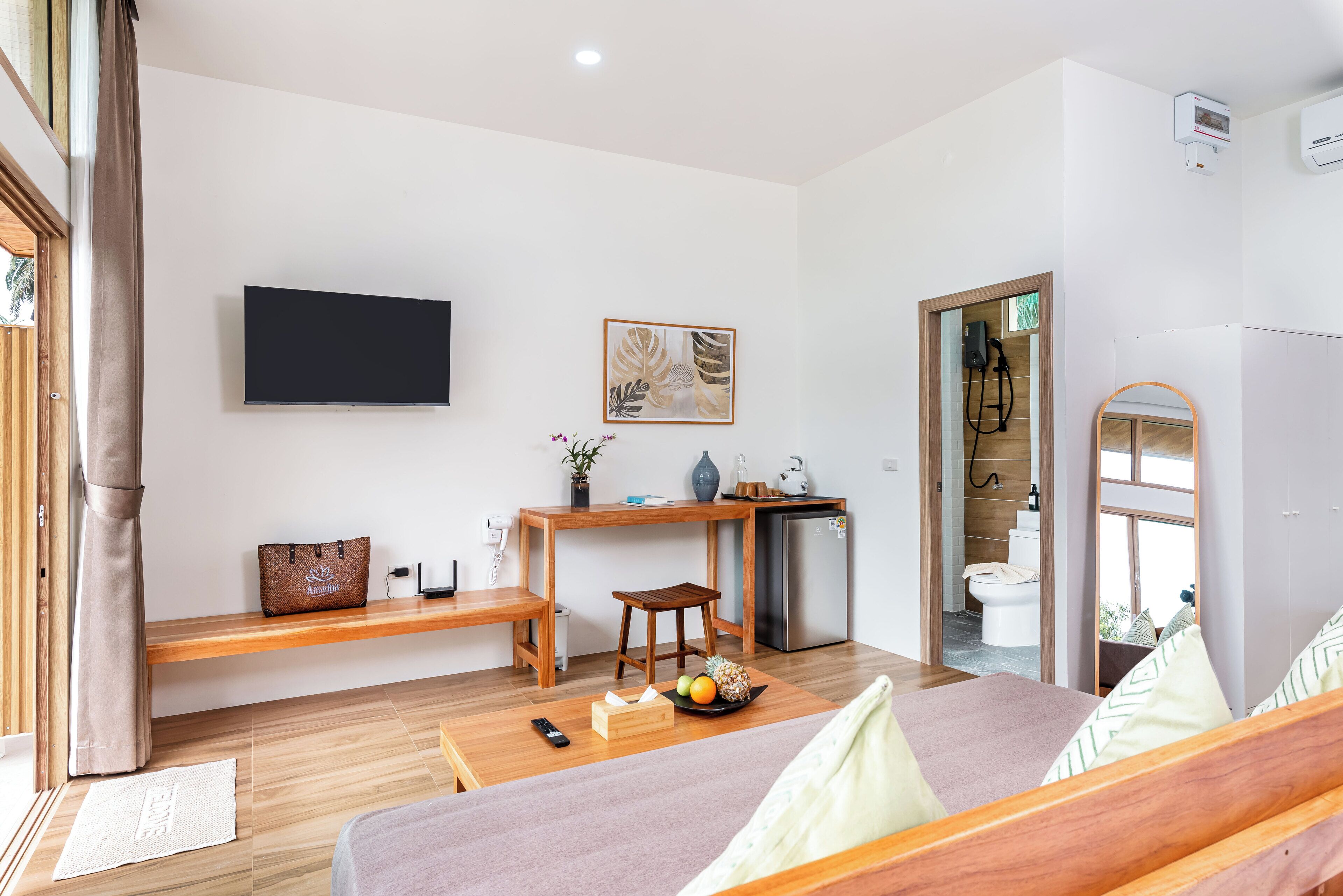A modern room with a bed, a desk, a TV, and a bathroom visible through an open door.