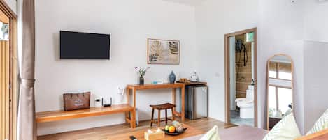 A modern room with a bed, a desk, a TV, and a bathroom visible through an open door.