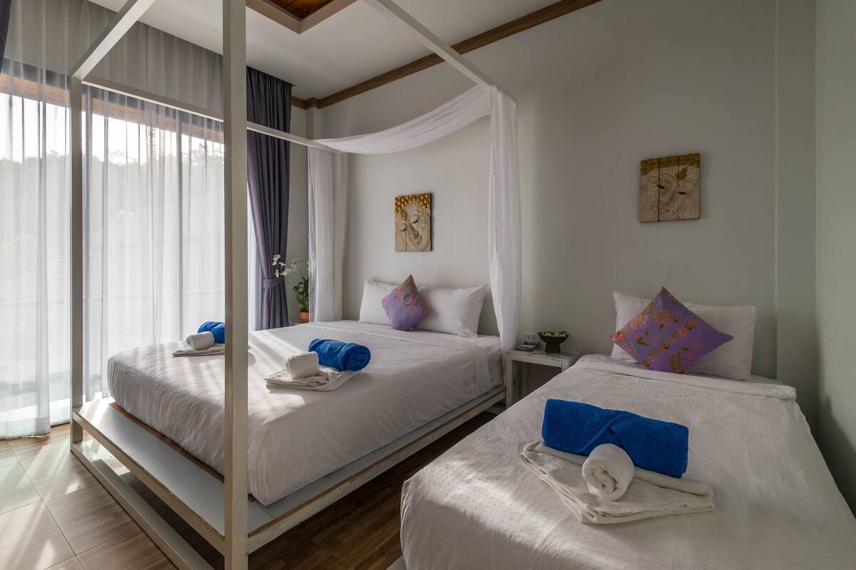 Une chambre d’hôtel avec deux lits, chacun agrémenté de draps blancs et de serviettes bleues. Deux tableaux sont accrochés au mur, et une petite table de chevet avec une lampe se trouve à côté de chaque lit.
