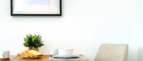 A dining area with a wooden table, two chairs, a potted plant, and framed artwork on the wall.