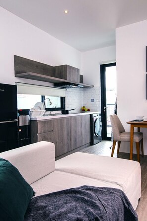 A modern kitchenette with a built-in oven, a sink, and a dishwasher. There is a dining area with a table and chairs.